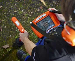 Technicien équipé d'un casque et d'un corrélateur acoustique pour repérer le bruit d'une fuite d'eau enterrée
